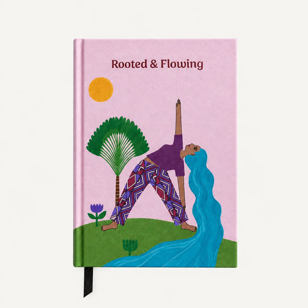 Load image into Gallery viewer, A hardcover journal titled 'Rooted &amp; Flowing' lies flat on a bed of dry brown autumn leaves. The cover features a light pink background with an illustration of a person in a yoga pose, green trees, a yellow sun, and a blue flowing shape.
