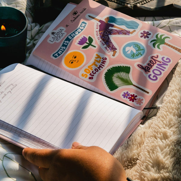 Load image into Gallery viewer, A hand holds an open lined notebook on a soft cream rug, with a pink sticker sheet featuring tropical and motivational designs placed on top. The sticker sheet includes illustrations of palm trees, flowers, a sunset, and phrases like 'This is enough' and 'Keep Going'.
